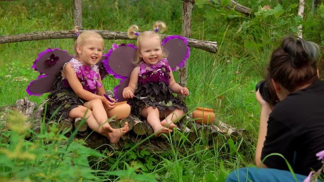 Female photographer takes pictures of beautiful girls playing violet butterflies. Girls smile and wear handmade butterfly wings and