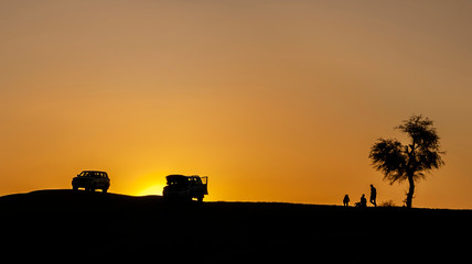 Black silhouettes of people, cars and a tree on the sunset - Sand dunes of a desert