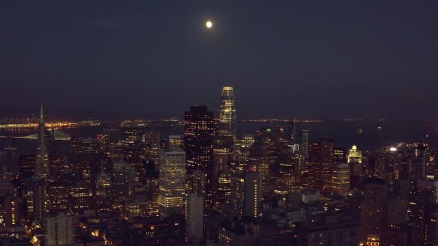 Aerial, rising, drone shot tilting towards skyscrapers in San Francisco downtown, during full moon, in California, USA