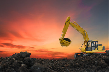 Excavators are digging the soil in the construction site on the orange  sky background - obrazy, fototapety, plakaty
