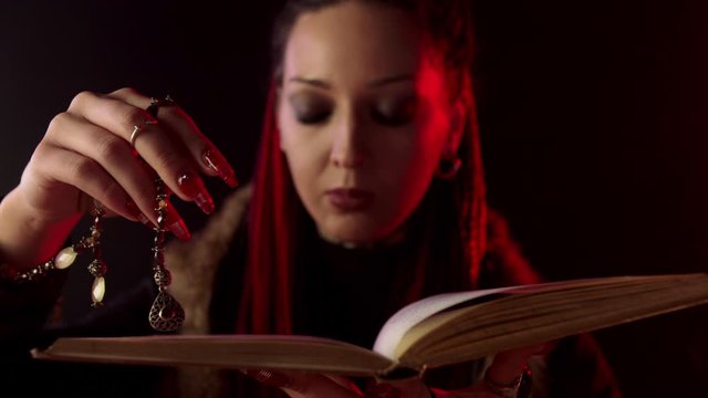 Witch with amulet reading magic book on black background