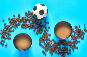 Full black cardboard glass of coffee near scattered beans and football, soccer ball on blue background. Concept of break, recreation, sport. Top view