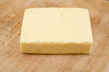 piece of hard cheese on a wooden background.