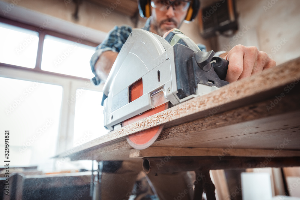 Wall mural carpenter using professional circular saw to cutting a wooden board in carpentry workshop