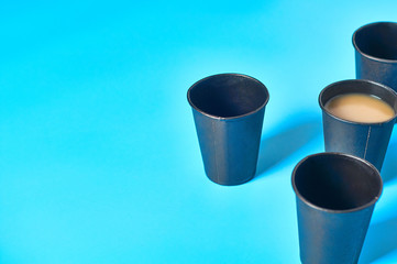 One full and many empty black cardboard glasses for hot beverages on blue background. Copy space. Concept of environmental protection, coffee break, ecology, garbage recycle