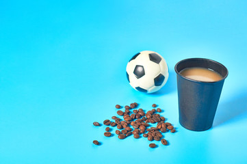 Full black cardboard glass of coffee near scattered beans and football, soccer ball on blue background. Copy space. Concept of environmental protection, break, ecology, recreation, sport