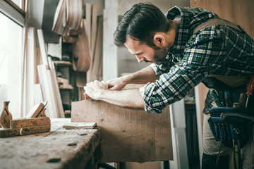 Carpenter planing a wooden board with a manual planer in carpentry workshop