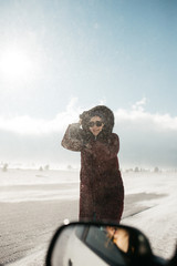 Image of pretty woman walking in snowy mountains. Portrait of female wearing warm winter jacket and walking in snowy road while the wind is blowing.