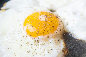 Fried egg close-up: whole yolk in focus. The concept of fried food, breakfast. Egg sprinkled with pepper.