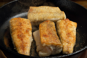 Frying portions of fresh fish in a black cast iron pan