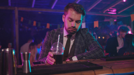 Portrait of exhausted businessman relaxing after hard working day drinking alcohol cocktail at bar counter in modern nightclub.
