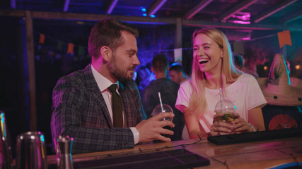 Successful romantic meet-up at night party. Businessman and young girl sitting at bar counter getting acquinted drinking cocktails having good time.