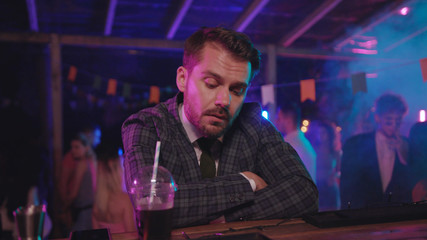 Tired young businessman falling asleep of alcohol on bar counter trying to stay awake on modern party in the night pub.
