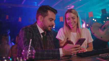 Fototapeta na wymiar Handsome businessman and a happy girl laughing of funny memes on smartphone sharing exciting stories chilling together at bar counter.
