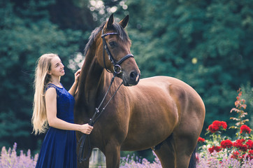 Teenager steht mit seinem Pferd im Kleid in einem Garten
