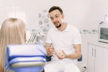 The dentist tells how to care for braces using the example of an artificial jaw. A woman, a dentist client, sits in a dental chair and listens to a doctors story about oral hygiene