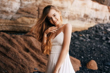 Fototapeta premium Gorgeous girl in a long white dress on the ocean at the beach. The model is inherited by nature laughing, having fun, going crazy. Happy girl on vacation, summer, emotions. The bride on vacation.