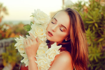 Beautiful portrait of a girl with white roses. Girl holds a bouquet of gorgeous roses near her face. Unification with nature, love.