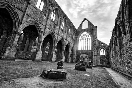Black and white photo of The ruins of Tintern Abbey, founded by Walter de Clare, Lord of Chepstow, on 9 May 1131. It is situated adjacent to the village of Tintern in Monmouthshire, Wales, UK.