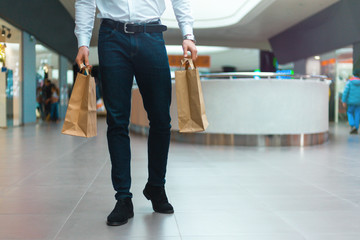 Young stylish man walking in a mall with ecology friendly shopping bags in hands with goods and...