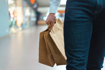 Fototapeta premium Closeup of a young stylish man walking in a mall with ecology friendly shopping bags in hand with goods and clothes. Sales, discount sold out concept. Seasonal sell out.