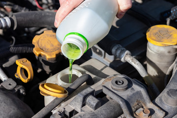 Hand with bottle pouring antifreeze coolant into the expansion tank. Dusty details of a flat-four...