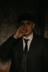 A man smokes a cigarette in the image of an English retro gangster in Peaky blinders style.