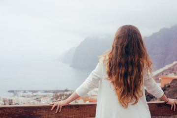 Woman on a background of mountains and a city. Girl travels in Tenerife. The girl in the summer knows the world. Great traveling, happy with long hair. Summer.