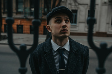 A man posing in the image of an English retro gangster in Peaky blinders style at city street.