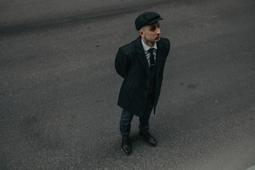 A man posing in the image of an English retro gangster in Peaky blinders style at city street.