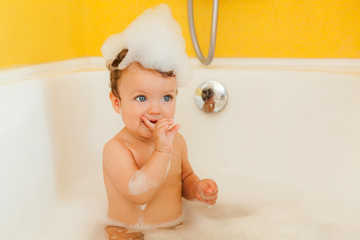 Smiling kid with foam and soap bubbles in bathroom.