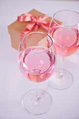 Two glasses with pink grape wine and gift box on the background. Romantic dinner concept.