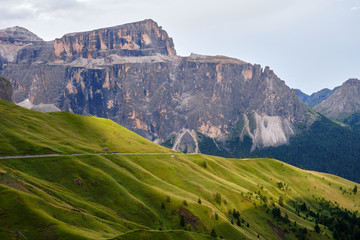 Sella mountain group in Dolomites, Italy, at sunset, with rays of light across green layers of grass.