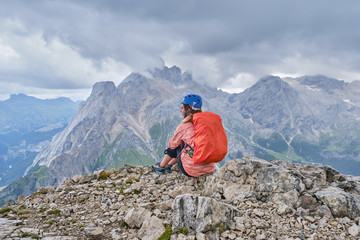 Woman on Colac peak, at the end of via ferrata dei Finanzieri, with helmet on and a backpack with rain cover, enjoys the panoramic views, with storm clouds approaching.