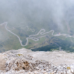 Winding road in fog at Pordoi pass, Dolomites mountains, Italy. View from high above on via ferrata route Eterna Brigata Cadore.