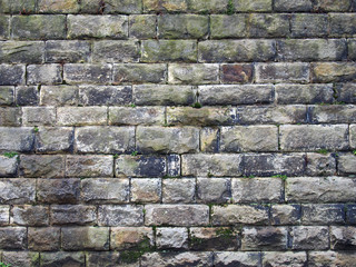 an old grey damp stone wall made of large regular blocks covered in patches of moss