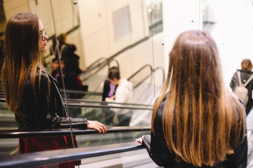 Young woman looking in mirror while standing on escalator in shopping mall