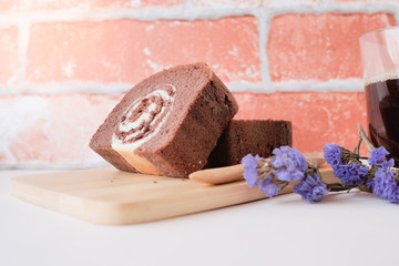 Close-up of chocolate jam roll on a wooden plate, there is a cup of coffee for blur background.