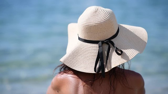 Back view of woman wearing straw hat on the beach, slow motion