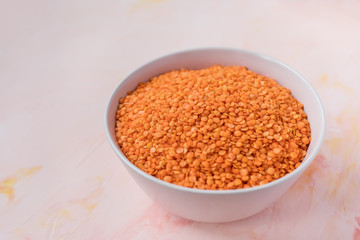 Raw red lentils in ceramic bowl on pink background, concept of healthy eating vegan food. Close up, selective focus, copy space
