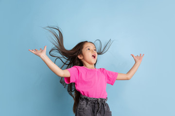 Astonished, flying hair. Caucasian little girl's portrait on blue studio background. Beautiful female model in pink shirt. Concept of human emotions, facial expression, sales, ad, youth, childhood.
