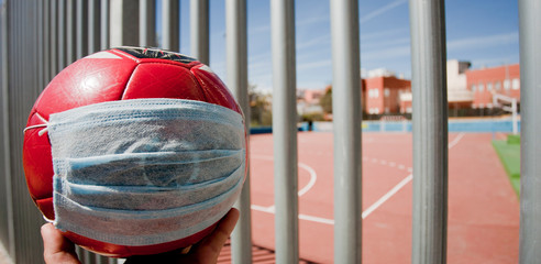 coronavirus concept in sport, soccer ball with breathing mask, closed soccer field fence