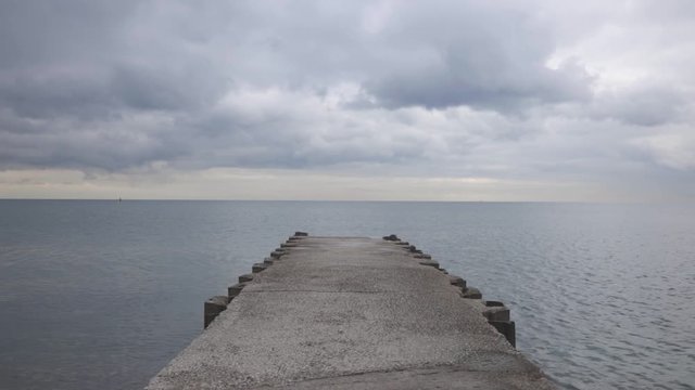 A narrow wharf facing towards the calm blue sea neath the white cloudy sky - static shot