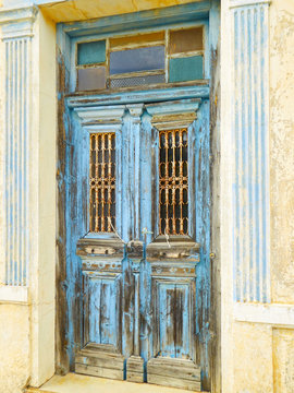 Weathered derelict blue wooden door with cracked paint at an abandoned rural house in Greece.