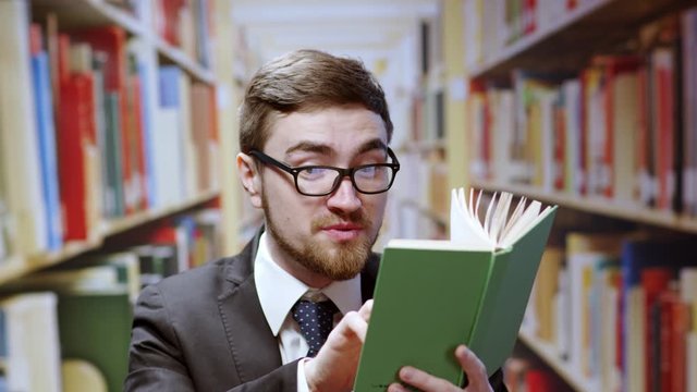 Handsome amazed man studying in the library reading books finds inpirational words quote smile satisfied enjoying posing on bookshelves background.