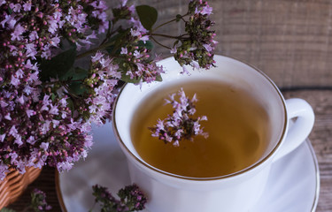 Herbal tea in a white Cup with oregano flowers, fresh oregano flowers on a background of wooden...