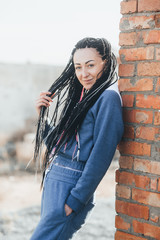 Girls in a blue suit with Senegalese Afro-braids, leaning against a red brick wall