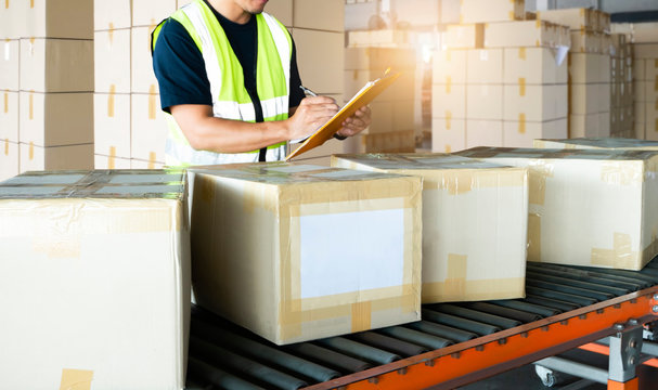 Warehouse worker holding clipboard writing on paper for shipment goods, package boxes sorting on conveyor belt, distribution warehouse delivery transport, logistics