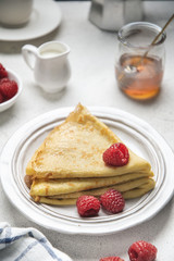 Crepes with raspberries and honey on white table