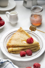 Crepes with raspberries and honey on white table